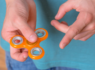 Male child hand holding popular fidget spinner toy - close up. Boy playing with a orange Spinner.