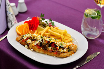Filet rybny z warzywami i frytkami podany na białym owalnym talerzu .