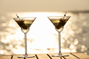 Two martini cocktails at the wooden pier at sunset. Luxury resort vacation concept. Festive relax getaway background.