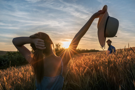 Woman and man with hats in wheat field with hands up