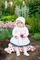 Girl 8 months old European Ukrainian little baby on a walk in the garden holds a flower and strawberries in her hands