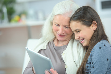 Granddaughter and grandmother laughing while looking at tablet