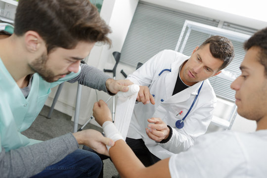 Student nurse bandaging patient's wrist under supervision