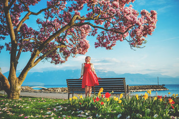 Young blond woman admiring amazing view of Lake Geneva, Switzerland. Woman sitting on the bench under blossom magnolia tree © annanahabed