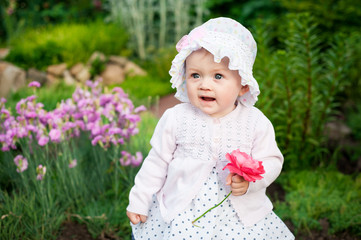 Girl 8 months old European Ukrainian little baby on a walk in the garden holds a flower and strawberries in her hands