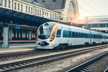 High speed train at the railway station at sunset in Europe. Modern intercity train on the railway platform. Industrial landscape with passenger train on railroad. Railway transportation. Locomotive