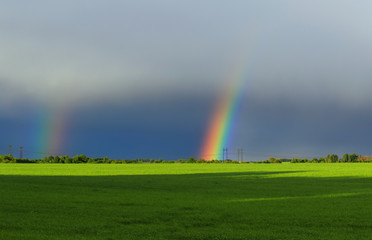 beautiful landscape with green meadow and a bright rainbow far away in the sky