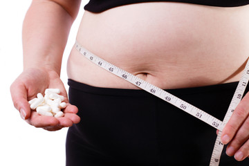 Young overweight unrecognizable woman with measuring tape around her waist and pills in hand