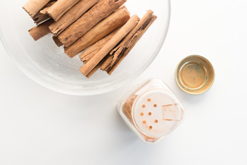 High angle close up view of cinnamon sticks in glass bowl and jar on white table (selective focus)