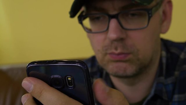 A Man In A Plaid Shirt Sitting On The Couch Using A Mobile Phone