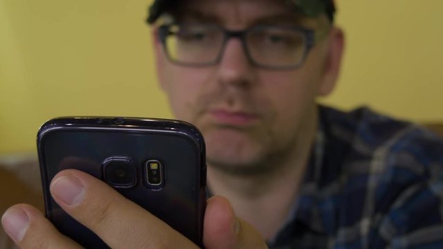A Man In A Plaid Shirt Sitting On The Couch Using A Mobile Phone