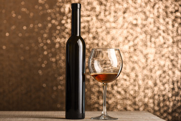 Glass with brown beverage near wine bottle on wooden surface