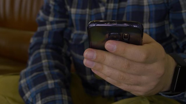 A Man In A Plaid Shirt Sitting On The Couch Using A Mobile Phone