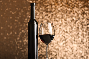 Glass of red wine near dark bottle on metallic background