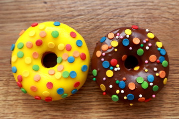Two assorted donuts on a wood background. Rainbow dots decoration. Brown sugar. Lemon, melon, pineapple, mango, banana flavour