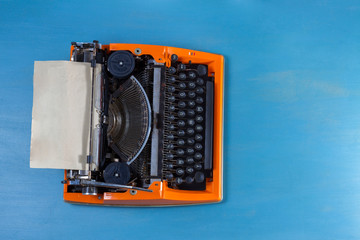 Workspace with orange vintage typewriter on blue background
