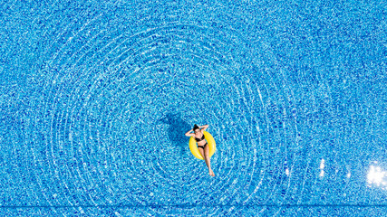 Aerial view of young brunette woman swimming on the inflatable big yellow ring in pool