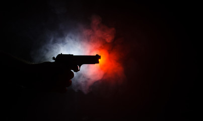 Fototapeta Male hand holding gun on black background with smoke ( yellow orange red white ) colored back lights, Mafia killer concept obraz