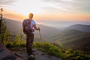Man tourist with trekking poles on top of hill at sunrise