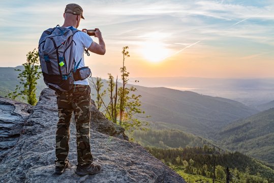 Man tourist on top of hill taking photo of sunrise