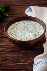 Okroshka. Summer light cold yogurt soup with cucumber, greens, eggs and dill on a wooden table. A traditional dish of Russian and Ukrainian  cuisine. Selective focus
