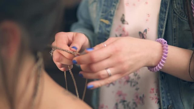 Closeup view of the hairdresser's hands doing dreads for a young woman in the hair salon. Shot in 4k