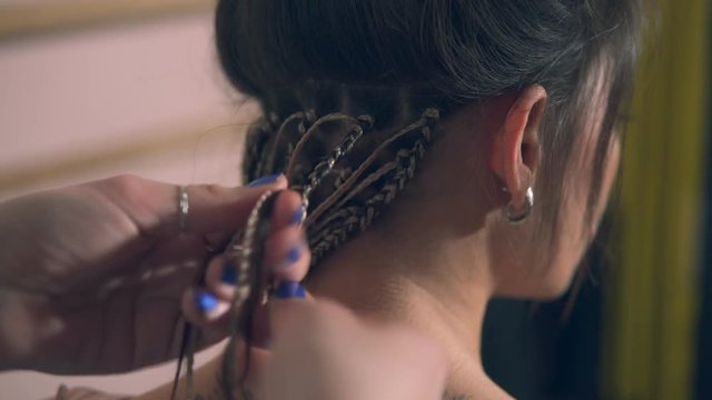 Closeup view of the hairdresser's hands doing dreads for a young woman in the hair salon. Shot in 4k