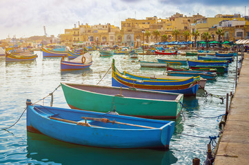 Fototapeta na wymiar Marsaxlokk, Malta - Traditional colorful maltese Luzzu fisherboats at the old village of Marsaxlokk with turquoise sea water and palm trees on a summer day