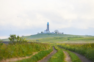 Fototapeta na wymiar Road to lighthouse in grass. Romantic landscape near black sea in summer field. Perfect landscape with light clouds and sand way in green field.