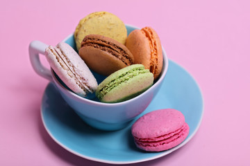 Colorful different flavored macaroons in a cup on pink background
