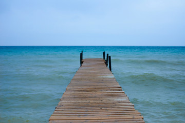 Fototapeta premium Wooden brown pier in waves sea or ocean in sunny day with horizon background and free space for advertising diving product. Perfect place for a fishing in relax time. Water energy on fresh air.