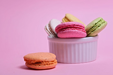 Colorful different flavored macaroons in a bowl on pink background