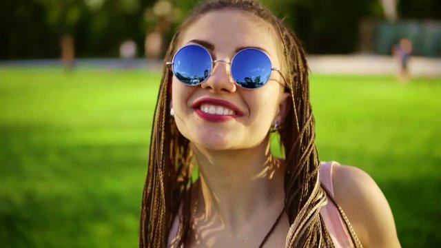 Young beautiful girl with dreads dancing in a park. Beautiful woman in jeans and sunglasses listening to music and dancing during a sunny day. Slowmotion shot.