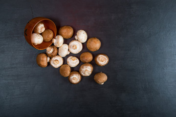 Fresh mushrooms champignon in wooden bowl on black background. Top view