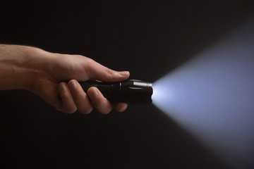 Black flashlight with wide beam in male's hand isolated from left side of the frame on black background - obrazy, fototapety, plakaty