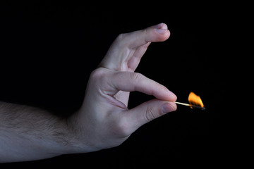 Men's black and white hand holding a burning match with a colored flame. isolated on black background closeup