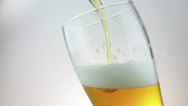 pouring fresh beer with foam into drink pint glass with ice frozen drops, shot slow motion on white background, fun and nutrition food and drink concept