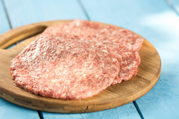 Raw minced meat burgers on the wooden round kitchen board