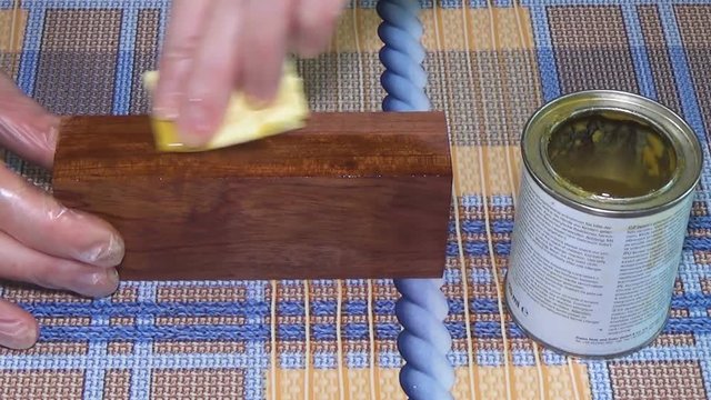 Wood beam palisander. The bar of solid wood is covered with stain. The girl covers a bar of rare wood with lacquer. The joinery impregnates the wood with wax. The end part of the wooden board.