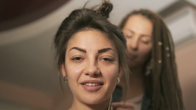 Closeup view of a young smiling hipster woman in the hair salon. The hairdresser doing dreads for a young woman. Slowmotion shot