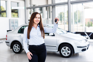 Fototapeta na wymiar Beautiful business woman standing in modern car dealership and holding car key