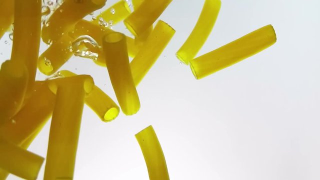 macaroni pasta splash falling into boiled water, shot in slow motion on white background, italian nutrition and health care concept