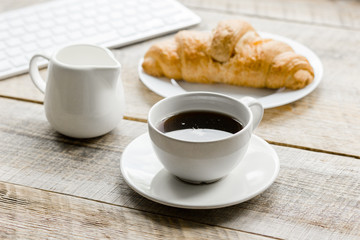 Businessman morning with keyboard, cup of coffee and croissant on wooden table background