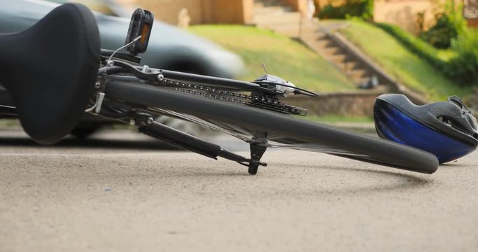A bicycle lays on the sidewalk with the wheels spinning after an accident as traffic passes by.	