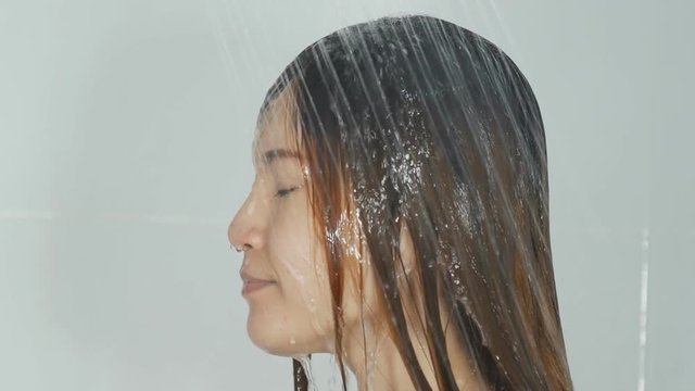 slow motion woman washing long hair in showering relaxing under running water in hot shower