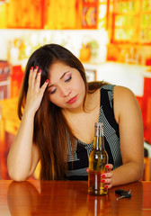 Portrait of a beautiful woman holding a beer with one hand and touching her head with her other hand, in bar background