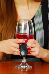Close up of a woman holding with both hands a glass of red wine and car keys over a wooden table