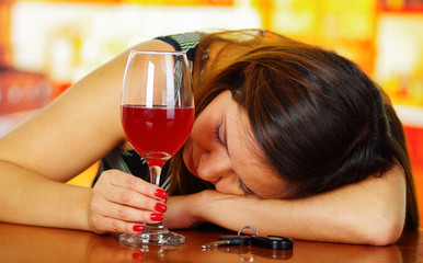 Portrait of a drunk woman sleeping over a wooden table and holding a glass of reed wine with her hand, in bar background