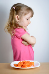 Little girl in the pink T-shirt refuses carrots. Problems of healthy eating - obrazy, fototapety, plakaty