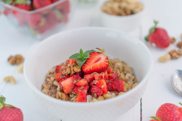 Summer healthy breakfast. Oatmeal with strawberries, walnuts, cashew nut, flax seed and mint on a white background on a wooden table. Cleansing the body. Products for weight loss. Wellness.